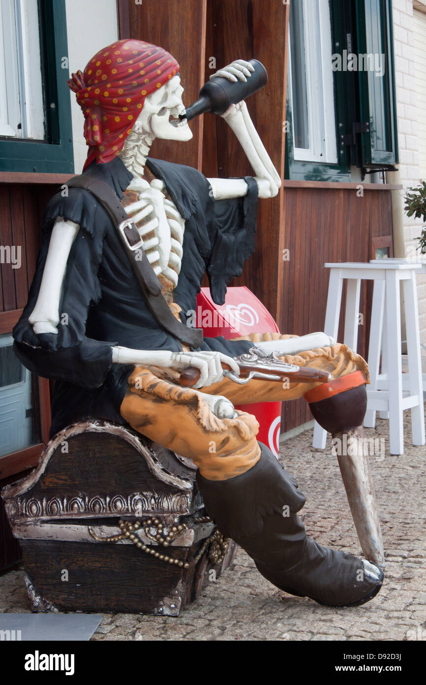 Full body pirate`s sculpture drinking holding a bottle and an old pistol, seated in a old treasure box Stock Photo